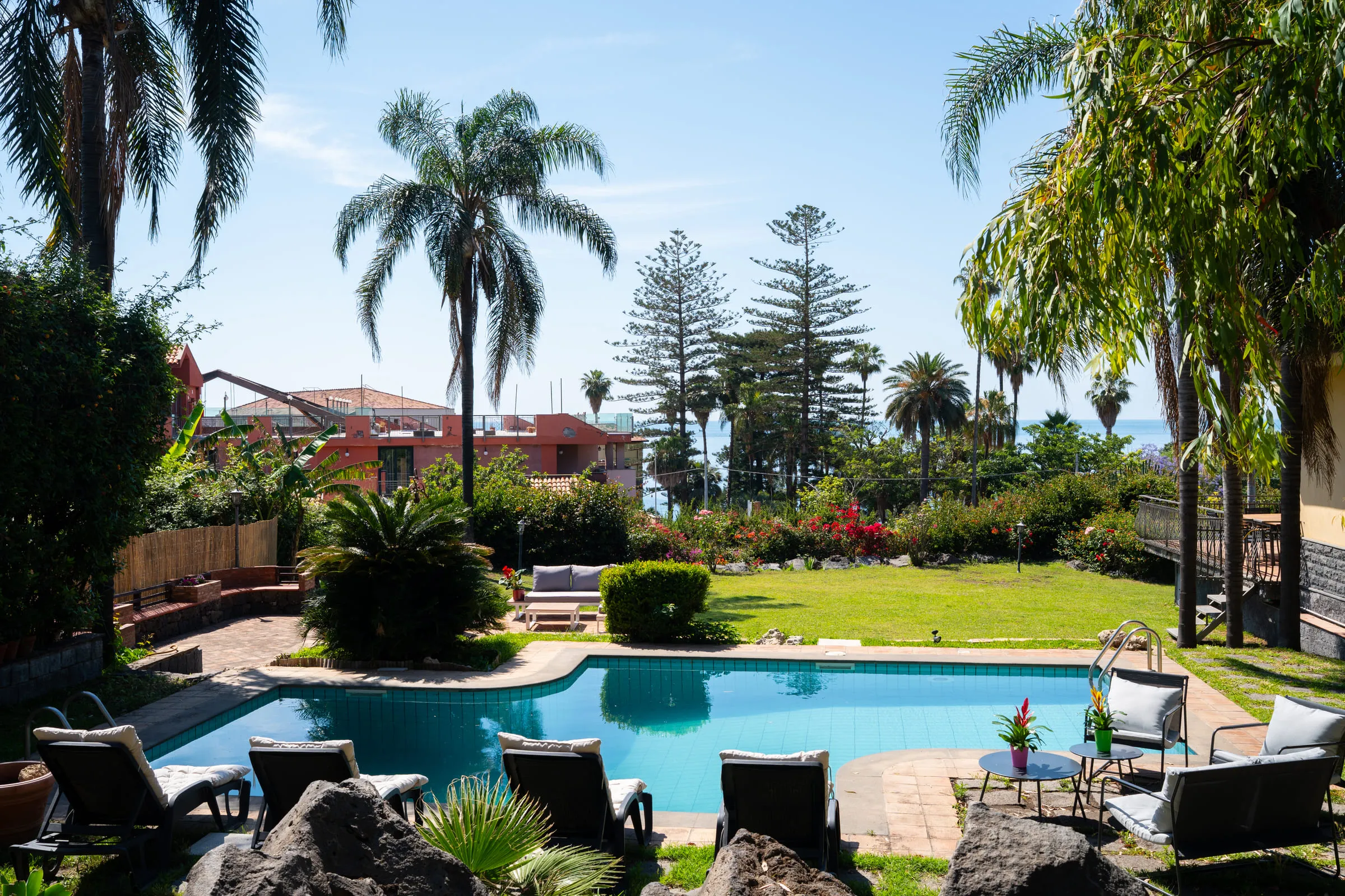 The garden seen from above, the pool in the foreground and the sea beyond the palms.
