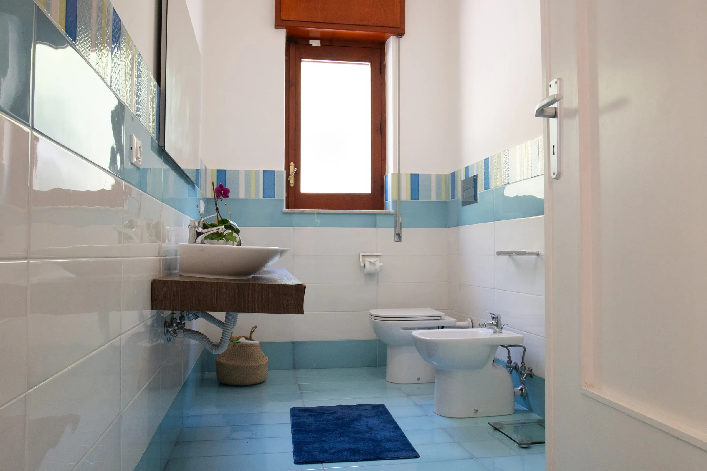 Bathroom with a countertop basin on a wooden shelf and pale blue tiling.