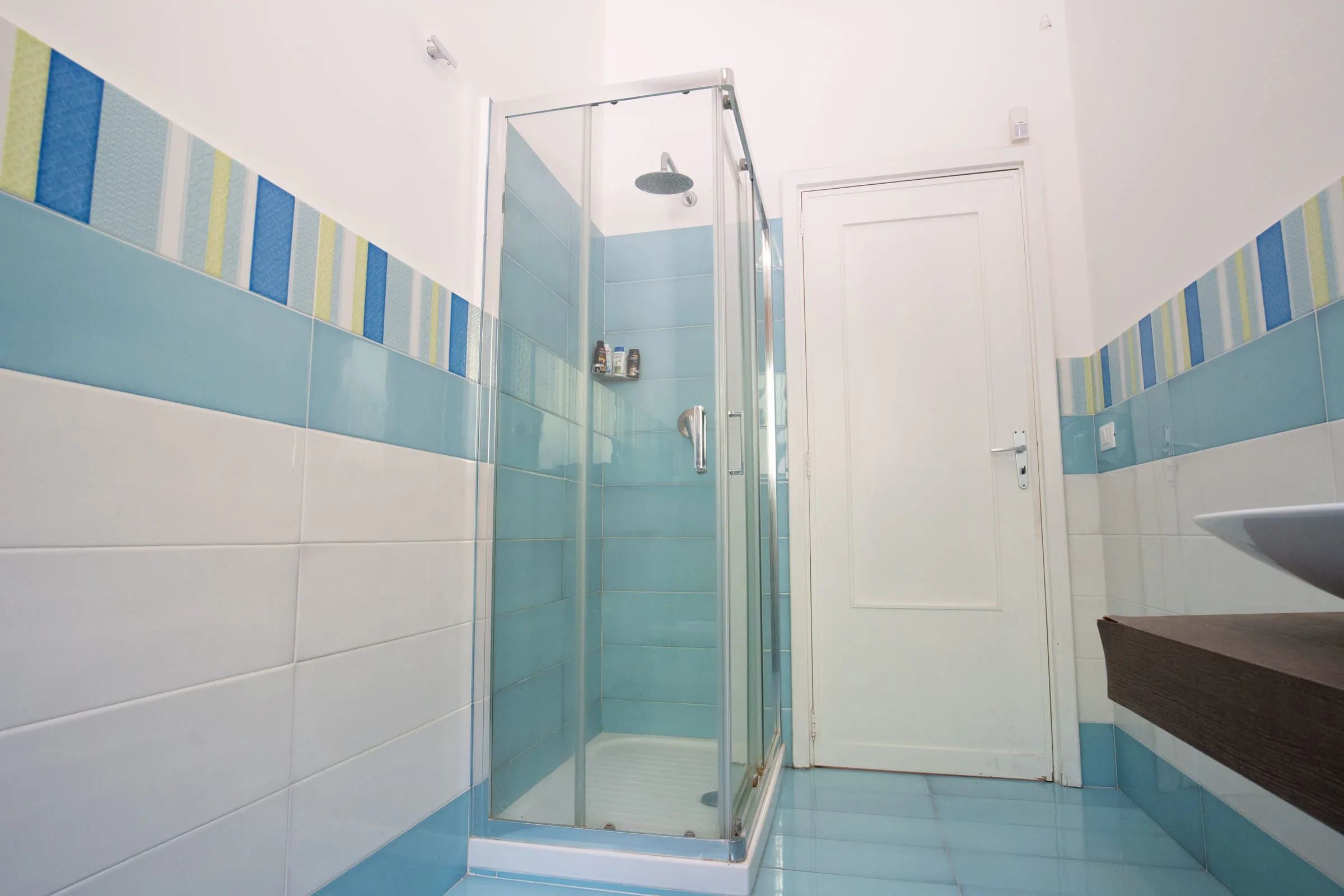 Glass shower enclosure in the pale blue tiled bathroom.