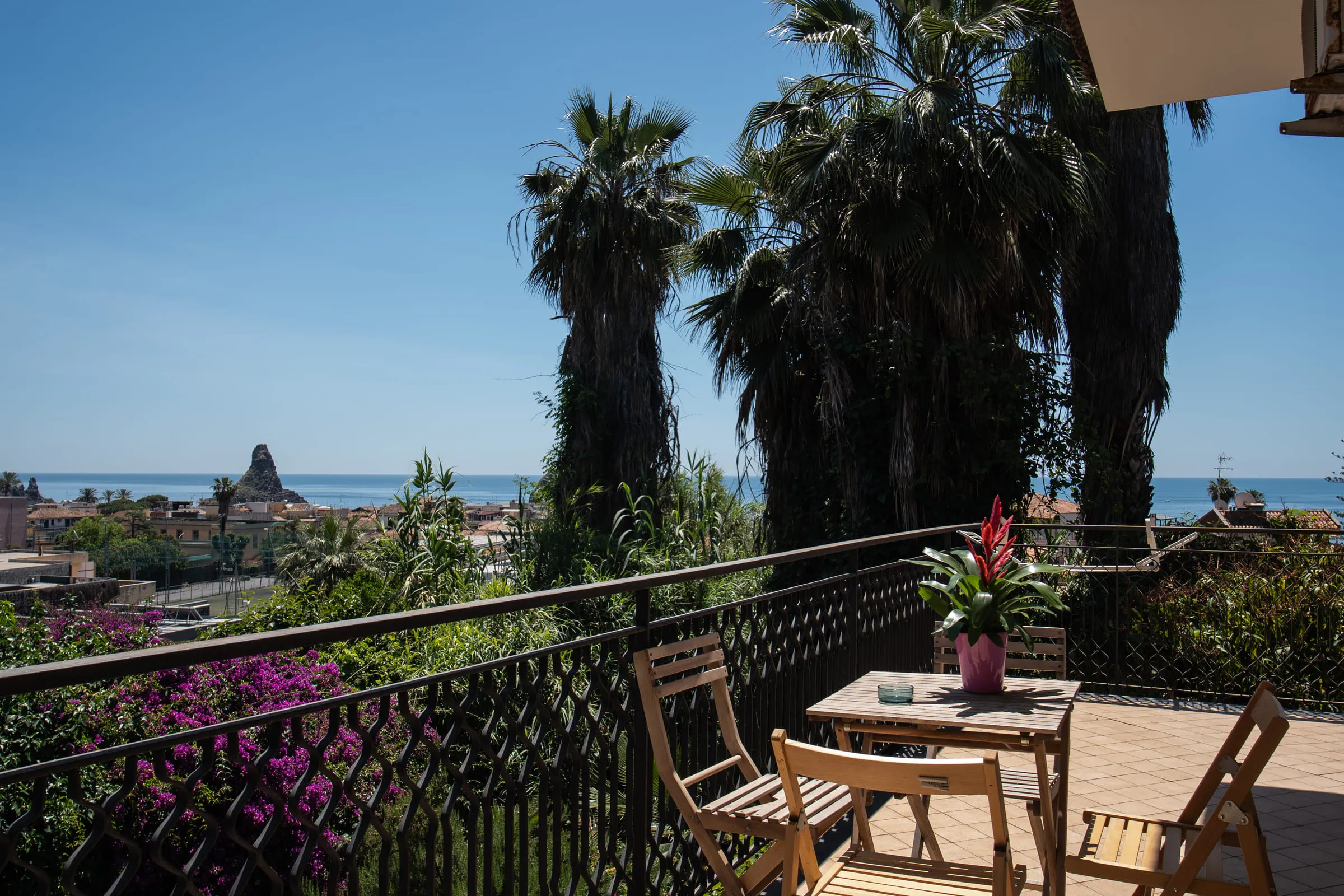 The balcony with its wooden table looking out over the faraglioni of Aci Trezza.