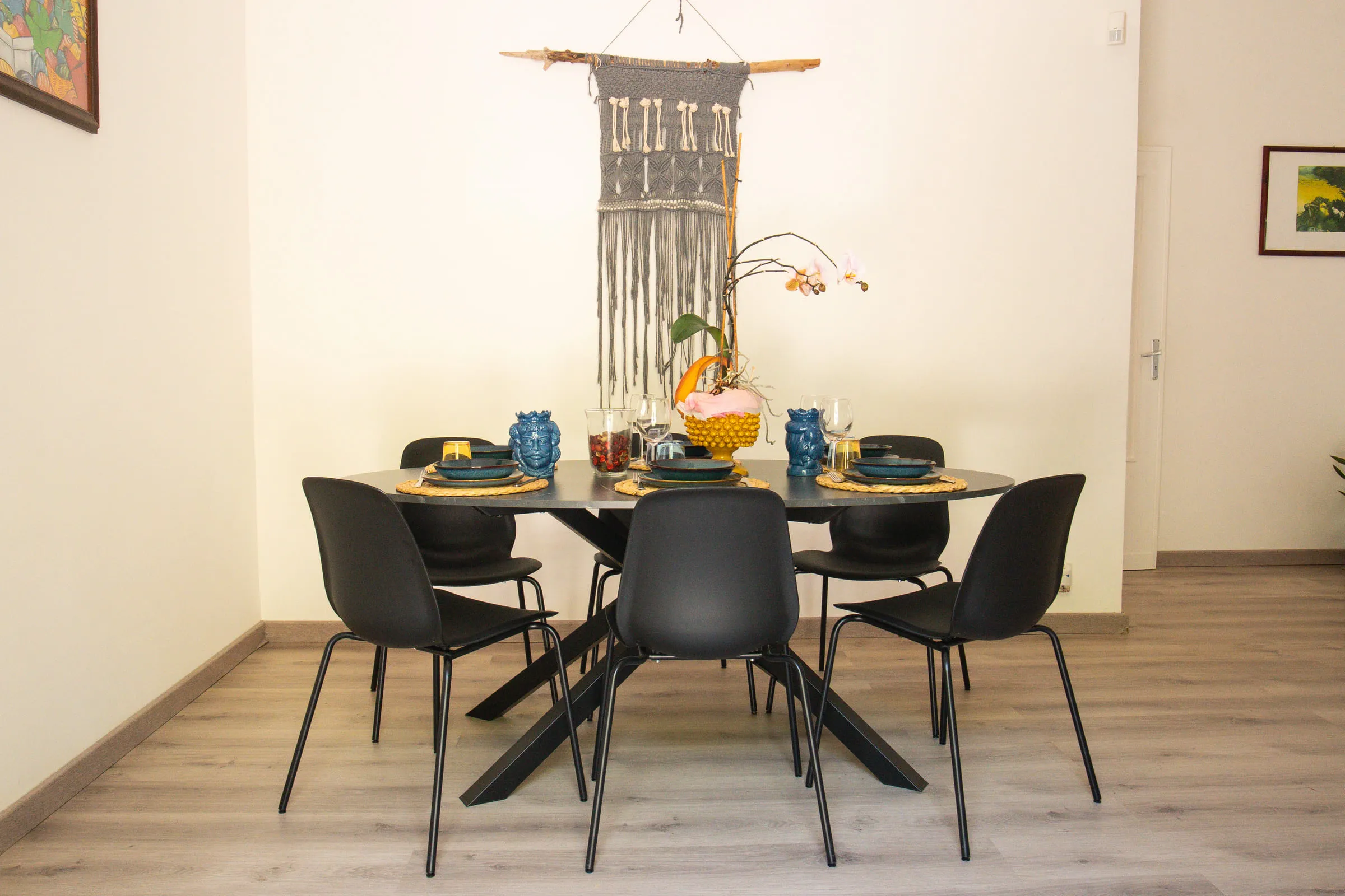 The round dining table with six chairs and a woven wall hanging.