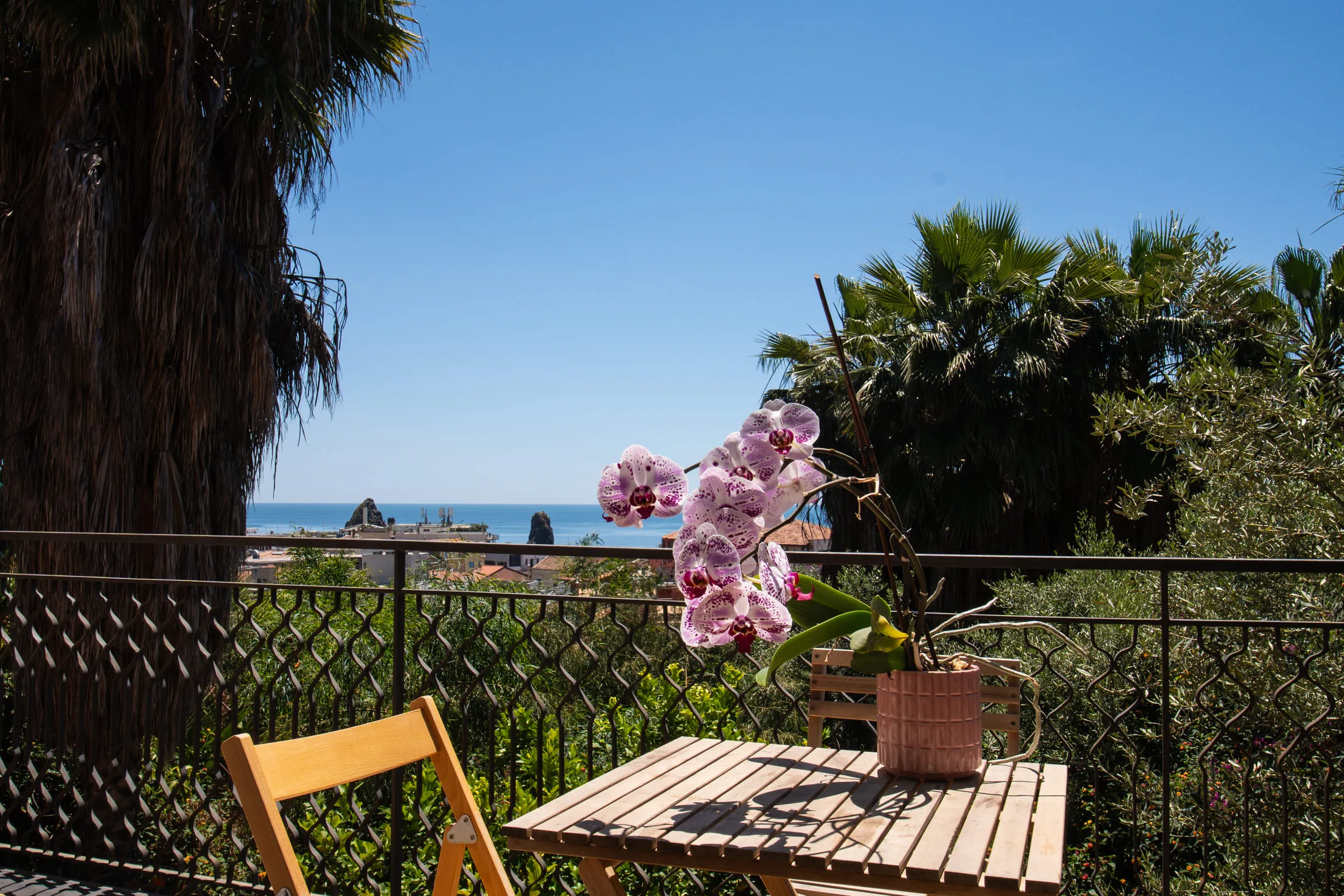 Small table and chair on the balcony, with orchids and the sea behind.