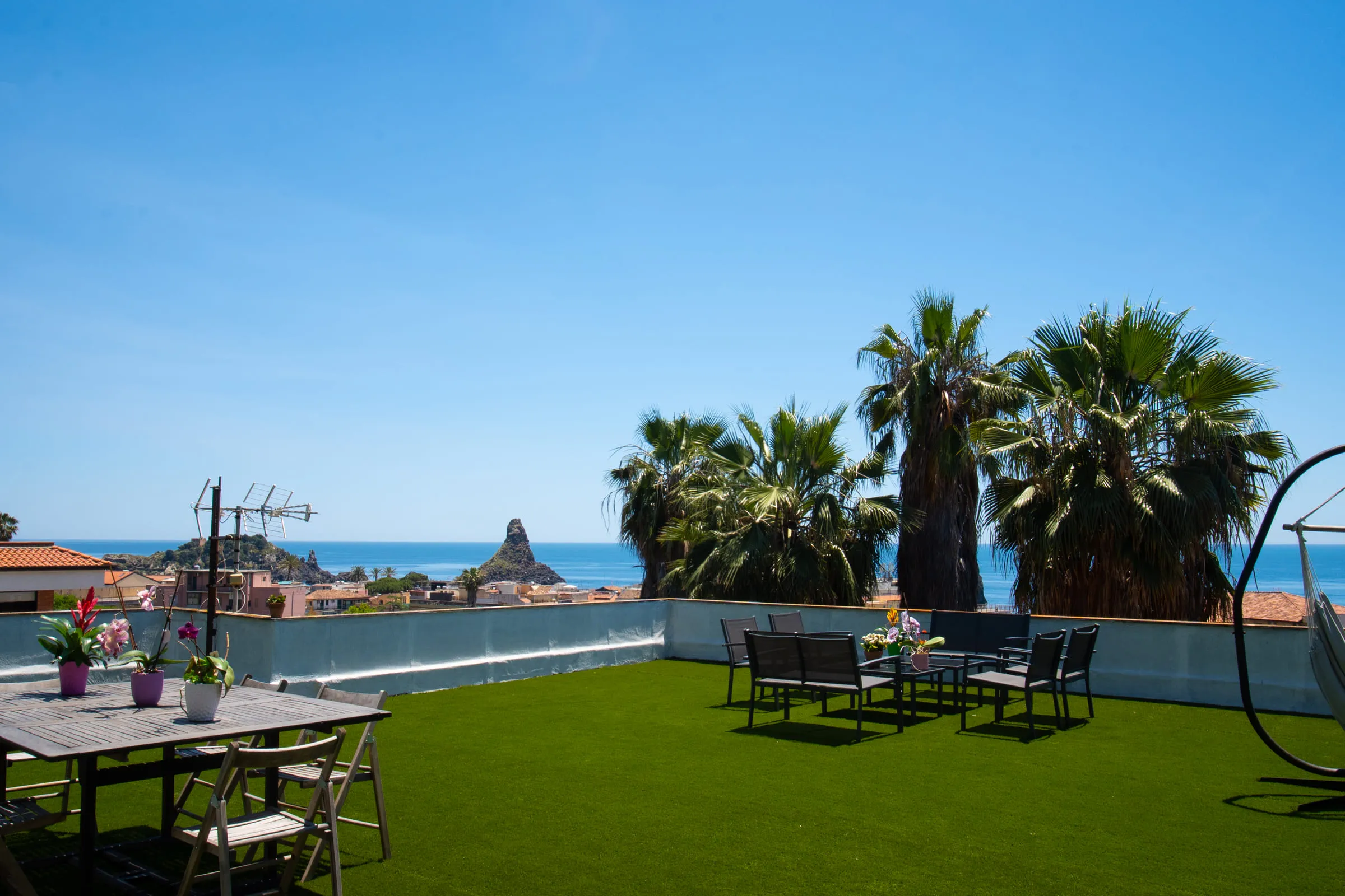 The terrace with the outdoor dining table, palms and the faraglioni on the sea.