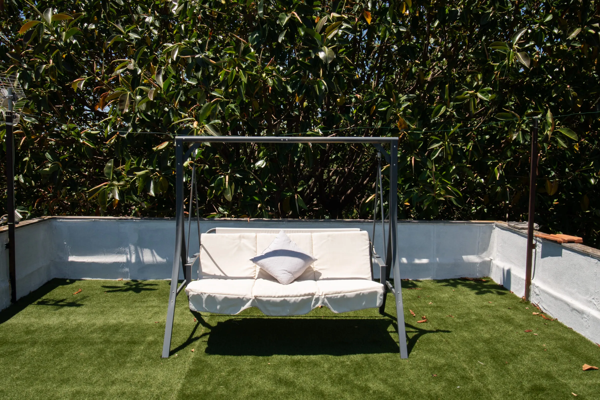 The white swing seat on the terrace, shaded by the hedge.