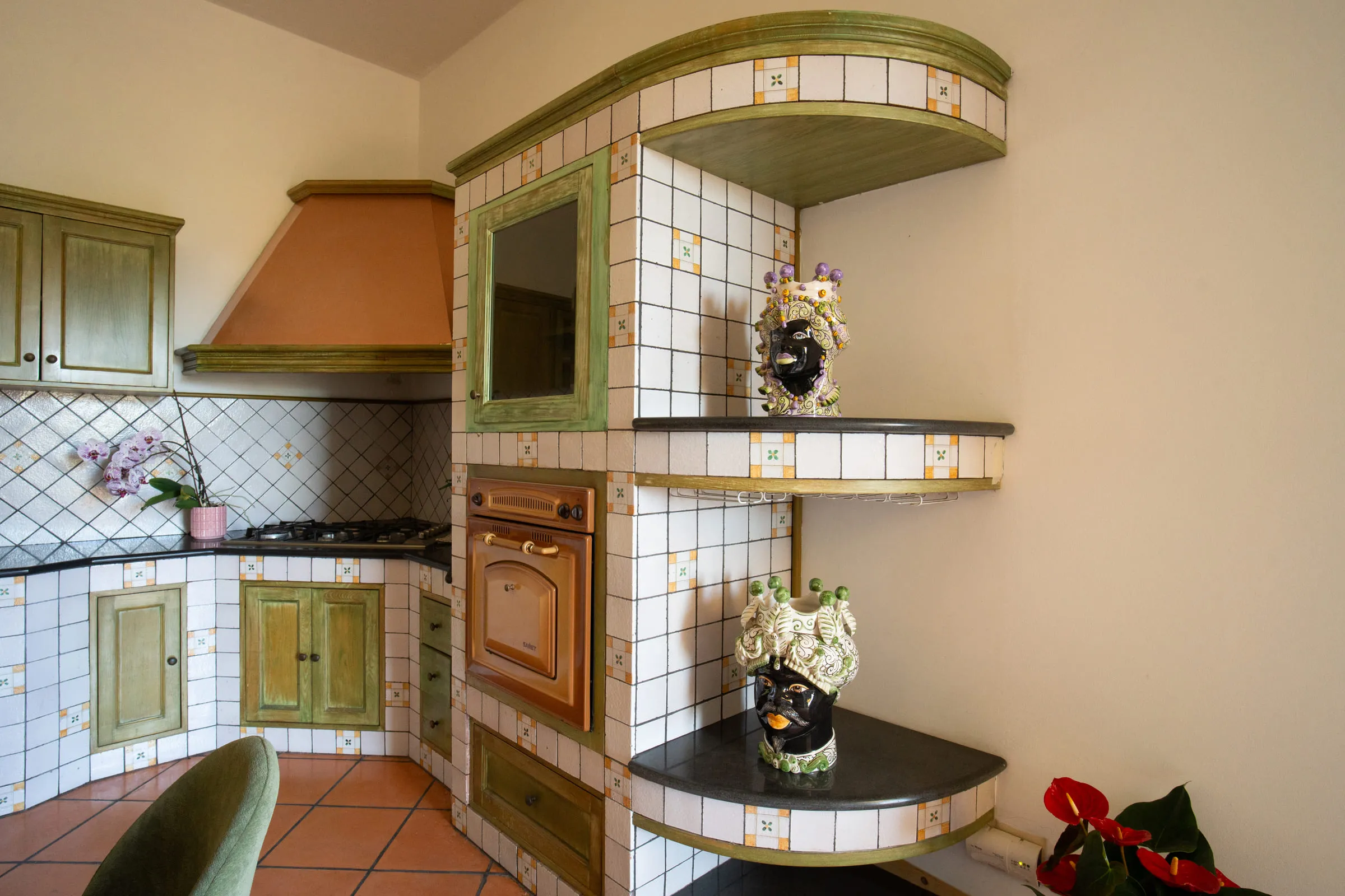 The tiled masonry kitchen, with the oven and ceramic teste di moro on the shelves.