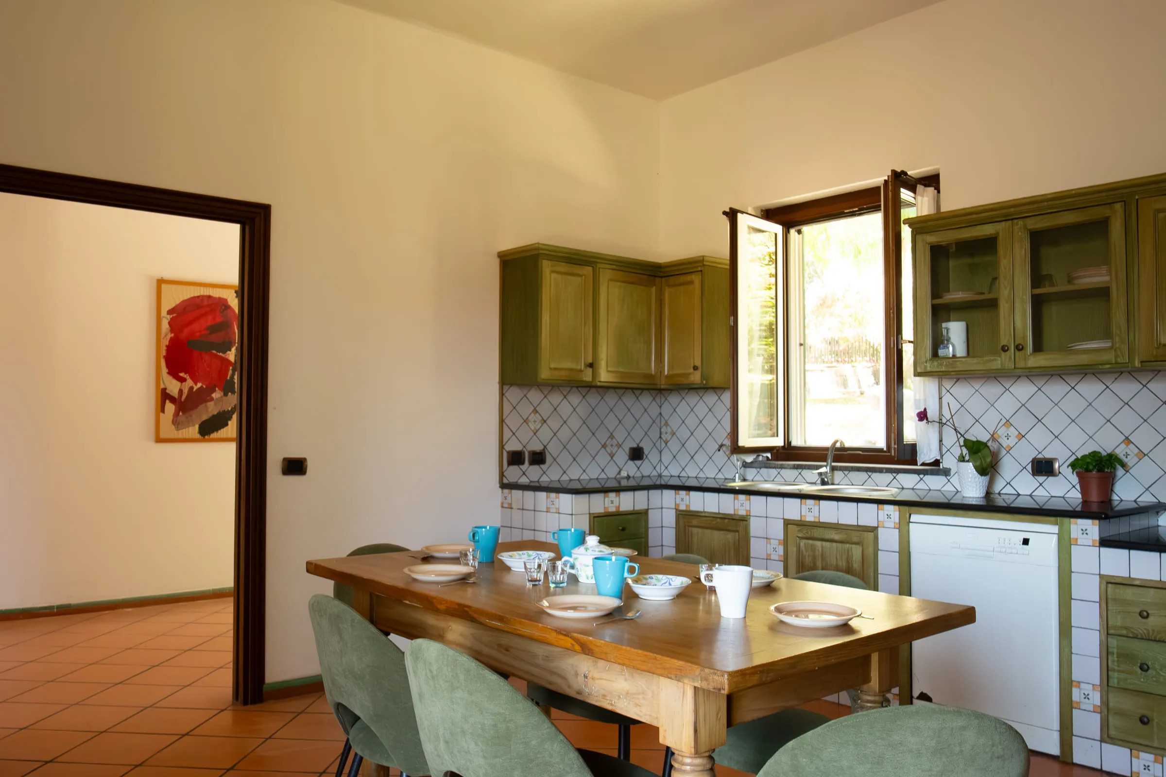 The kitchen with green cabinets and the wooden table laid.