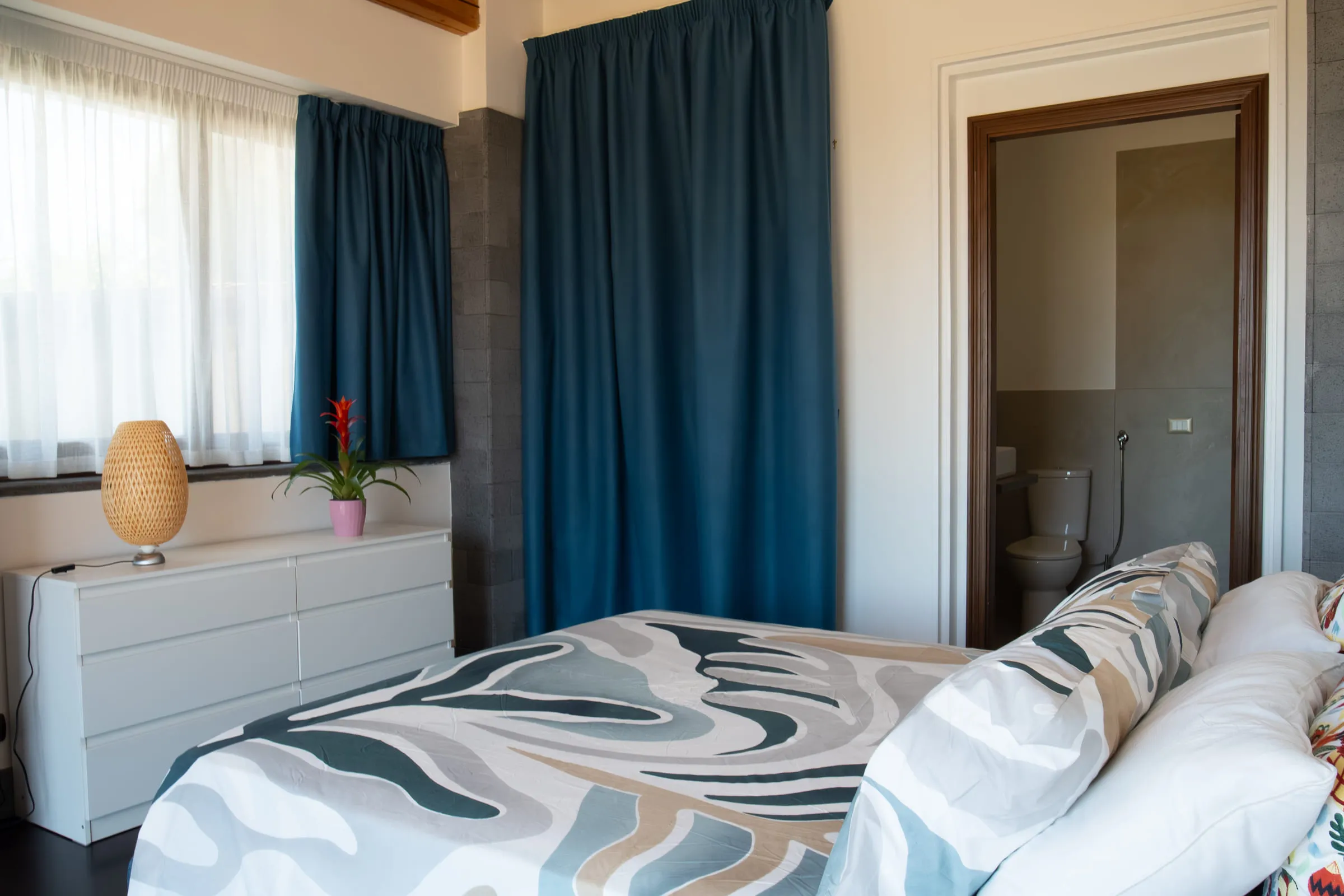 Double bedroom with blue curtains and the door to its private bathroom.