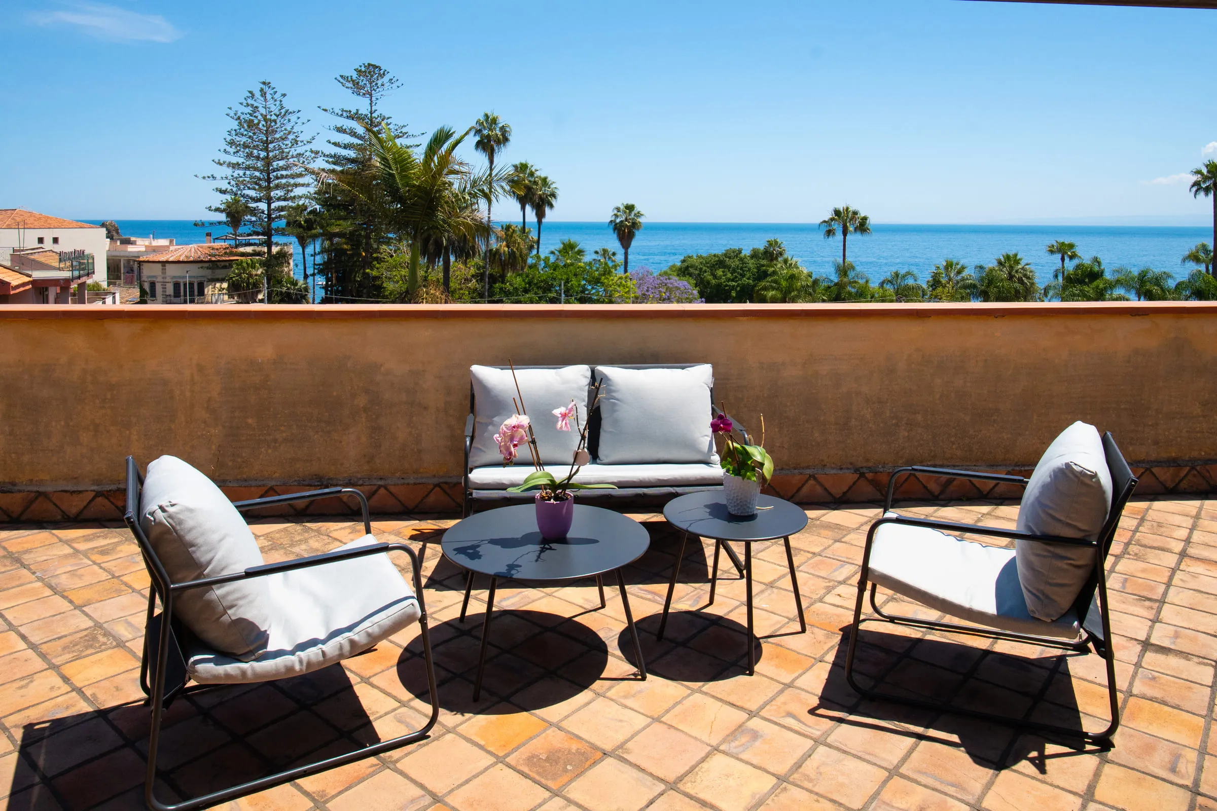 Outdoor sofa and armchairs on the terrace, pines and open sea ahead.