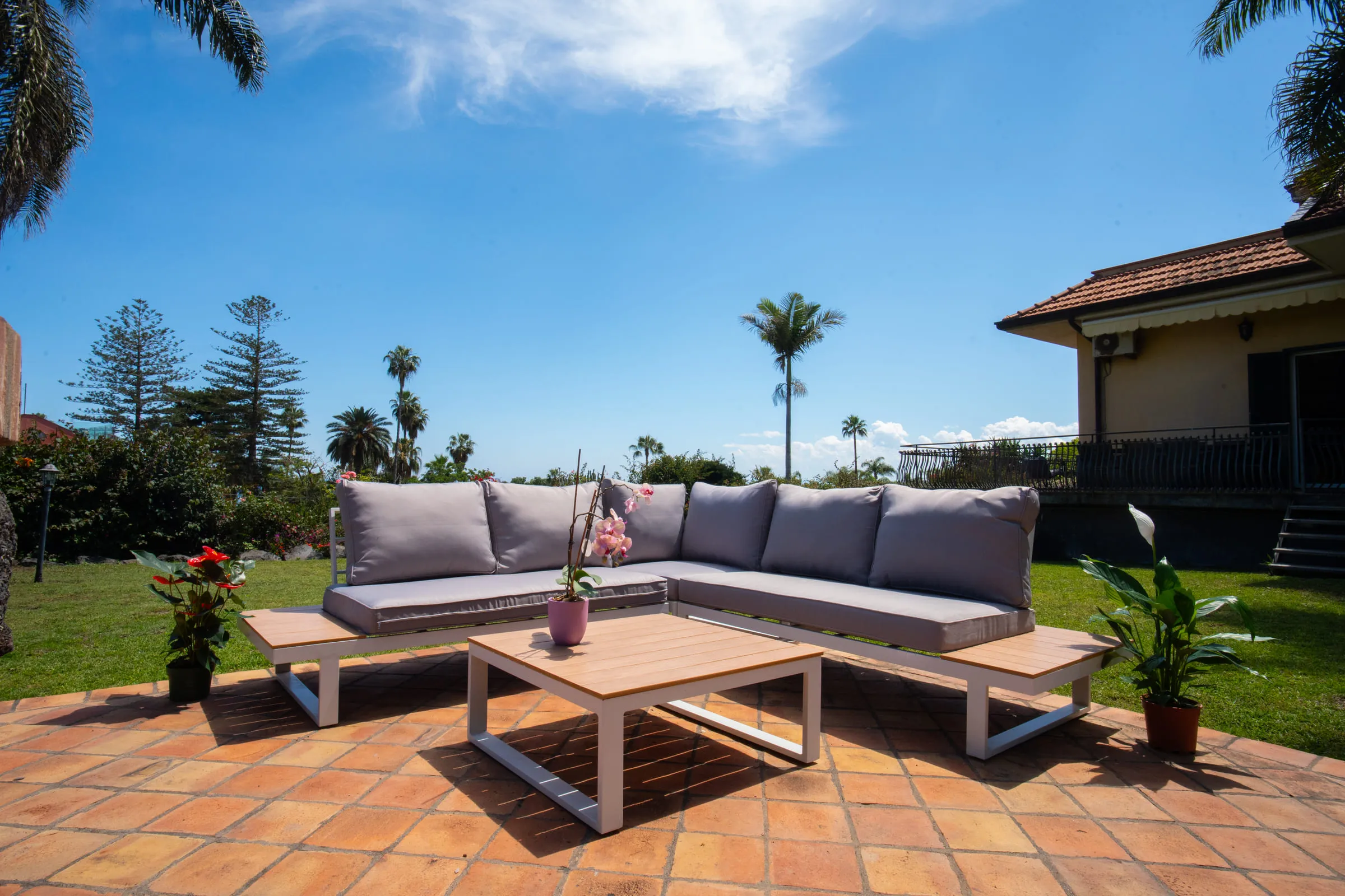 Corner sofa and low wooden table on the patio, under the palms.